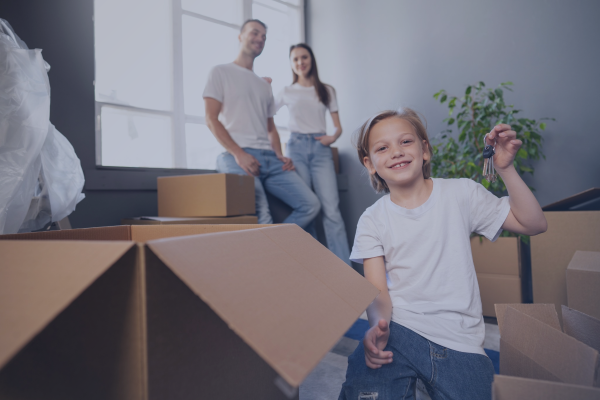 Smiling family moving into a new home with cardboard boxes, as a child holds house keys in the foreground, representing a residential mortgage and home ownership.